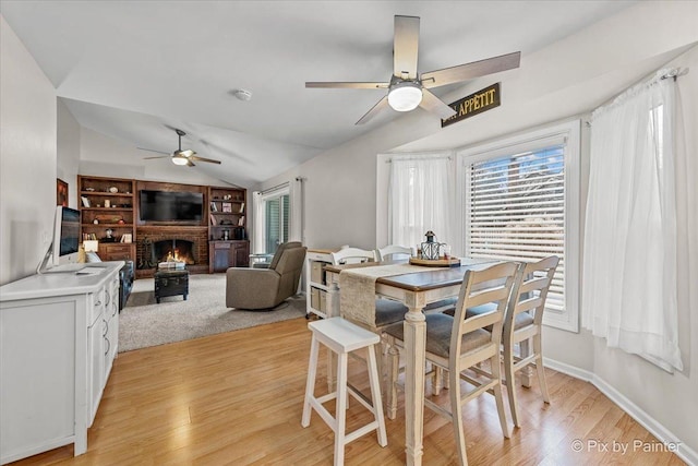 dining area featuring a brick fireplace, a healthy amount of sunlight, lofted ceiling, and light hardwood / wood-style flooring