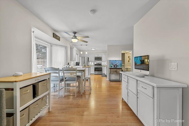 kitchen featuring light hardwood / wood-style flooring, ceiling fan, decorative light fixtures, white cabinetry, and stainless steel appliances