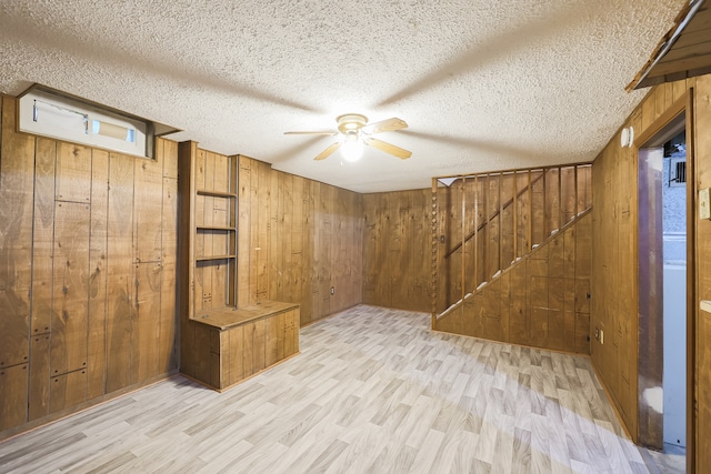 basement featuring ceiling fan, a textured ceiling, light hardwood / wood-style flooring, and wooden walls