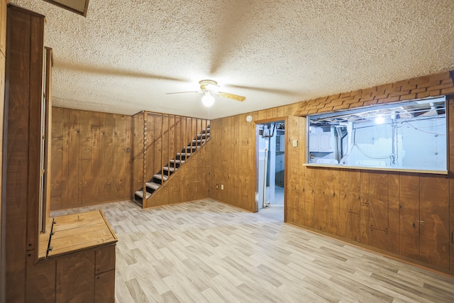 basement featuring light hardwood / wood-style floors, wood walls, a textured ceiling, and ceiling fan