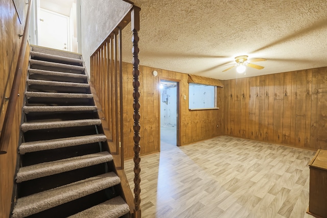 staircase with wood walls, hardwood / wood-style floors, a textured ceiling, and ceiling fan