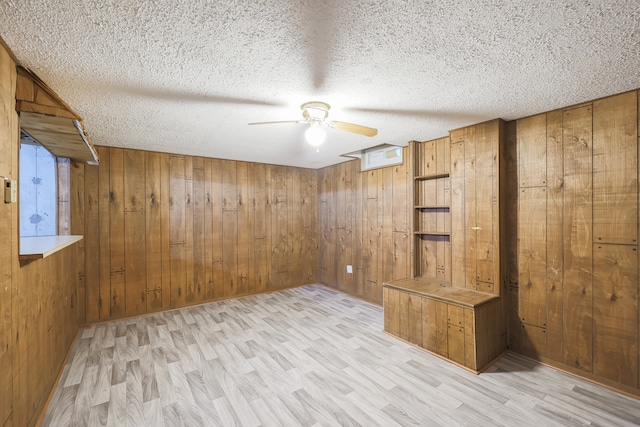 spare room featuring light hardwood / wood-style floors, a textured ceiling, wooden walls, and ceiling fan