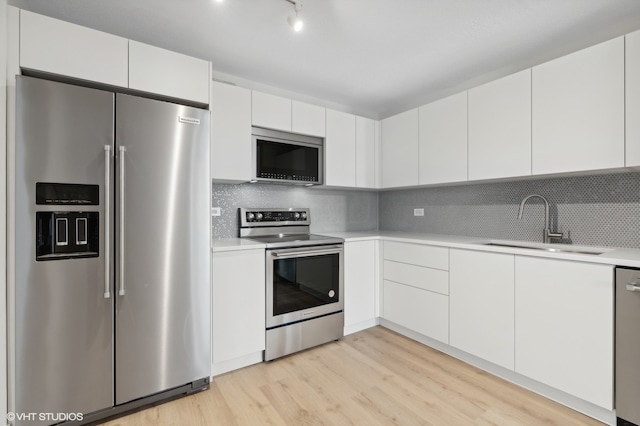 kitchen with appliances with stainless steel finishes, light hardwood / wood-style flooring, white cabinets, and sink