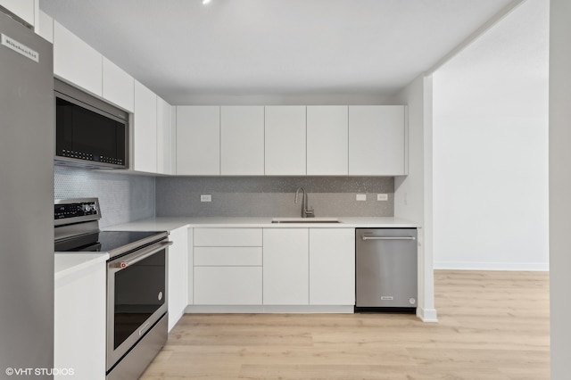 kitchen with light hardwood / wood-style flooring, backsplash, sink, white cabinetry, and appliances with stainless steel finishes