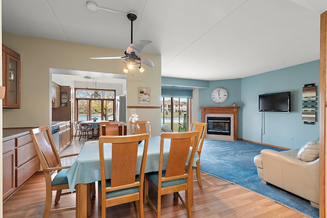 dining area with light hardwood / wood-style flooring, a tiled fireplace, and ceiling fan