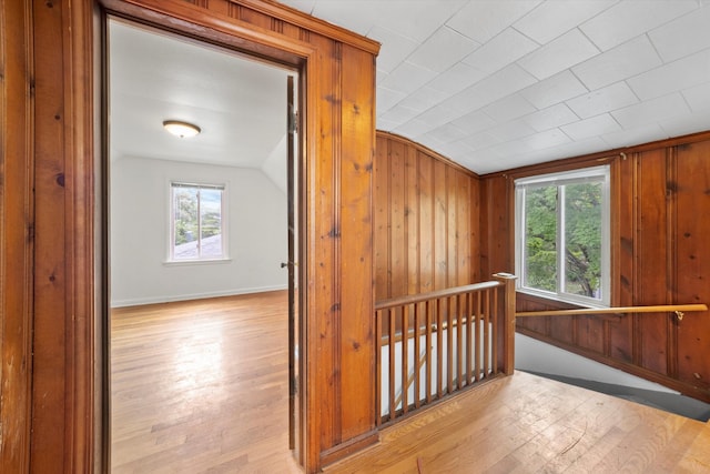 hall with light hardwood / wood-style floors, lofted ceiling, wood walls, and a healthy amount of sunlight