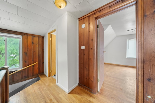 corridor with light hardwood / wood-style floors, lofted ceiling, and wooden walls