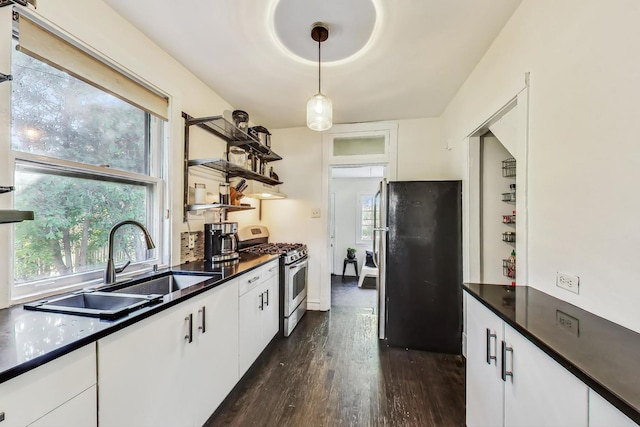 kitchen with dark hardwood / wood-style floors, stainless steel gas stove, black refrigerator, hanging light fixtures, and white cabinets