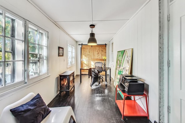 dining space with dark wood-type flooring, a wood stove, wooden walls, and a barn door