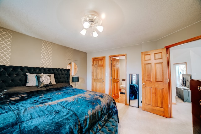 bedroom with a textured ceiling, light carpet, ensuite bathroom, and ceiling fan