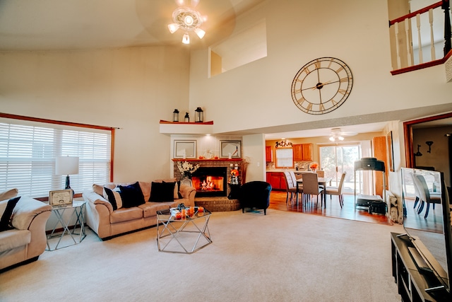 living room with ceiling fan, light carpet, a towering ceiling, and a brick fireplace