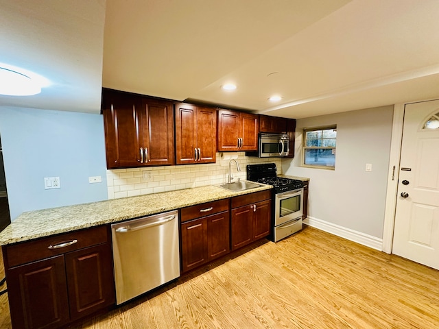 kitchen with stainless steel appliances, backsplash, sink, light stone counters, and light hardwood / wood-style floors