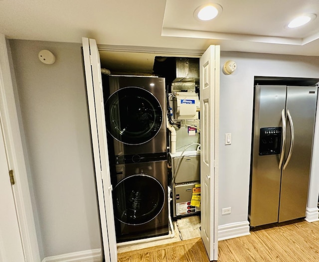 laundry room featuring baseboards, wood finished floors, stacked washer / drying machine, and laundry area
