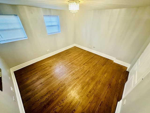 spare room featuring a chandelier, baseboards, and wood finished floors
