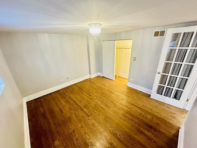 unfurnished room featuring an inviting chandelier, visible vents, wood finished floors, and baseboards