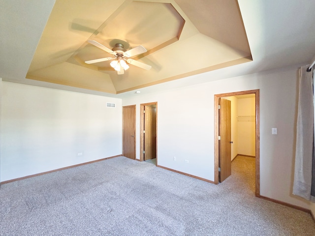 unfurnished bedroom featuring a spacious closet, ceiling fan, a raised ceiling, and light colored carpet