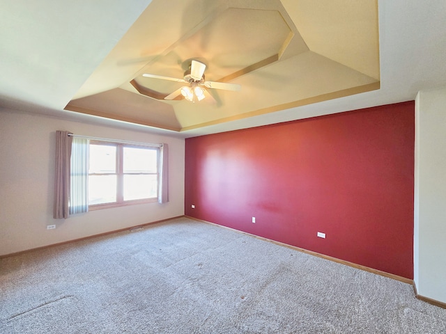 carpeted spare room featuring ceiling fan and a raised ceiling