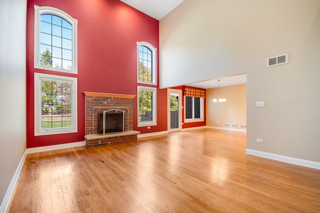 unfurnished living room featuring an inviting chandelier, light hardwood / wood-style flooring, a fireplace, and a towering ceiling