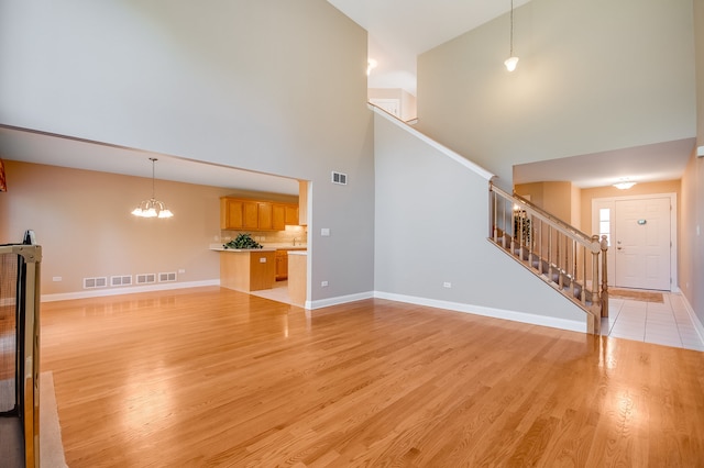 unfurnished living room with a notable chandelier, light hardwood / wood-style floors, and high vaulted ceiling