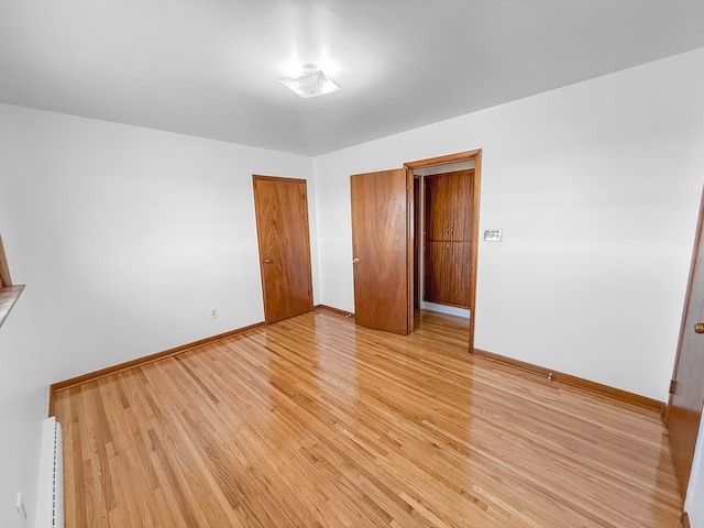 unfurnished bedroom featuring baseboard heating and light hardwood / wood-style floors