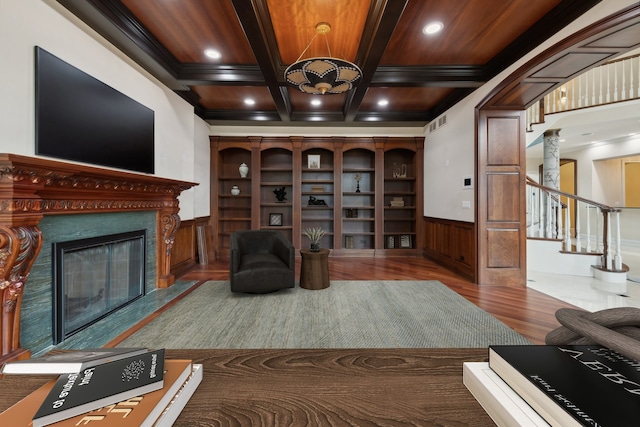 living room featuring a premium fireplace, hardwood / wood-style floors, a chandelier, coffered ceiling, and beam ceiling