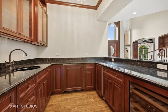 kitchen with dark stone counters, beverage cooler, sink, ornamental molding, and light hardwood / wood-style flooring