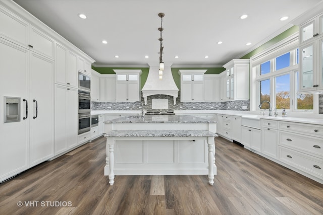 kitchen with an island with sink, custom range hood, pendant lighting, and dark hardwood / wood-style flooring