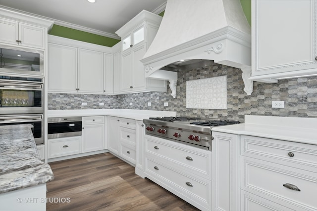 kitchen featuring stainless steel appliances, dark wood-type flooring, white cabinets, tasteful backsplash, and custom range hood