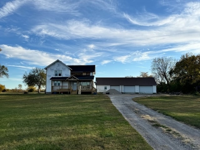 view of front of property featuring a front yard, covered porch, a garage, and an outbuilding