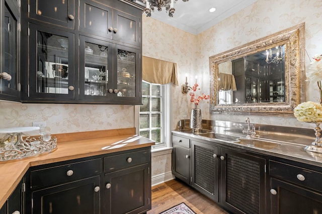 bar featuring an inviting chandelier, wallpapered walls, wood finished floors, indoor wet bar, and ornamental molding