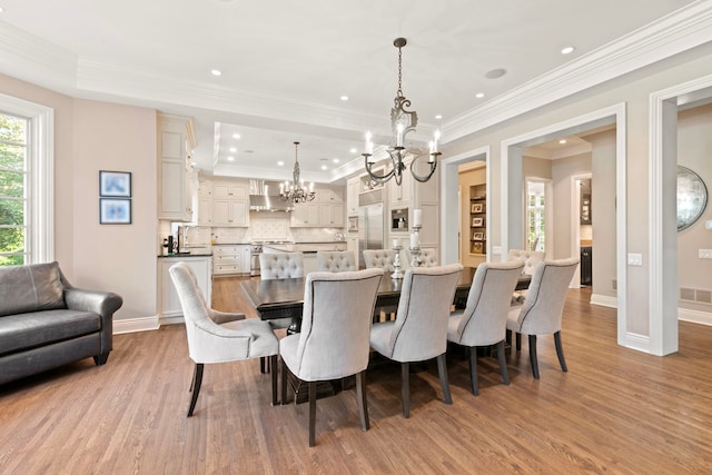 dining space with wood finished floors, a chandelier, a raised ceiling, baseboards, and ornamental molding