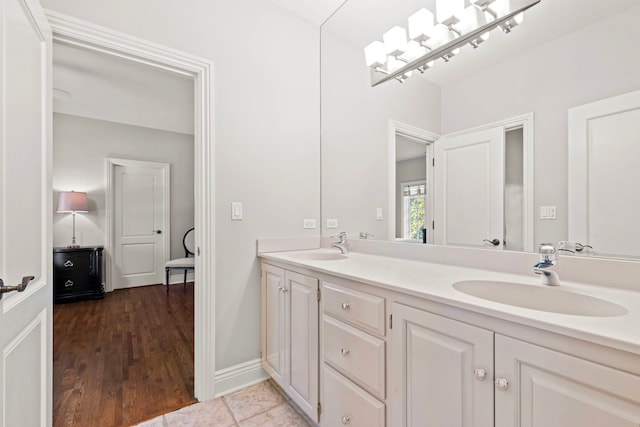 full bath with wood finished floors, baseboards, a sink, and double vanity