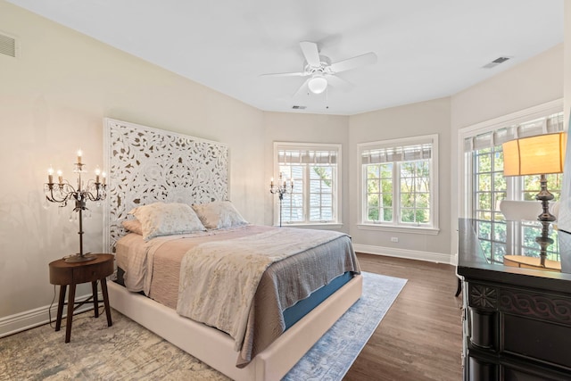 bedroom with visible vents, wood finished floors, baseboards, and ceiling fan with notable chandelier