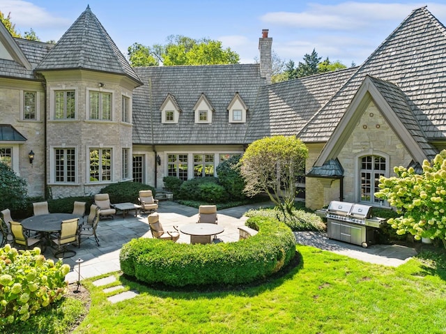 back of house with a chimney, stone siding, a patio area, and a yard