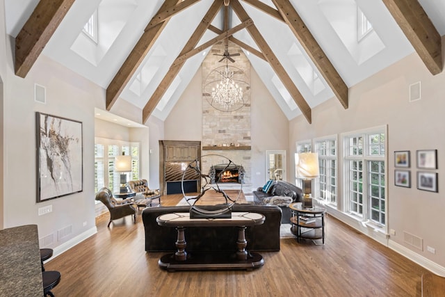 living area featuring high vaulted ceiling, a stone fireplace, a skylight, baseboards, and beam ceiling