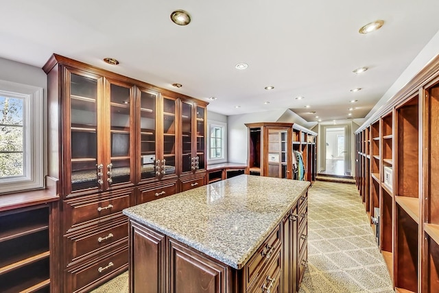 kitchen with a kitchen island, light stone counters, and light carpet