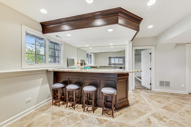 kitchen featuring kitchen peninsula, a breakfast bar, light stone countertops, and plenty of natural light