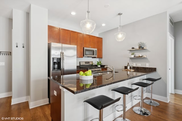 kitchen with appliances with stainless steel finishes, kitchen peninsula, dark stone counters, pendant lighting, and dark wood-type flooring