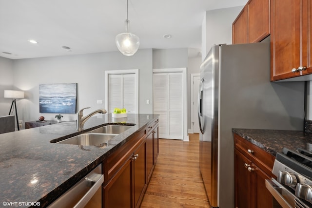 kitchen with stainless steel appliances, dark stone counters, sink, pendant lighting, and light wood-type flooring