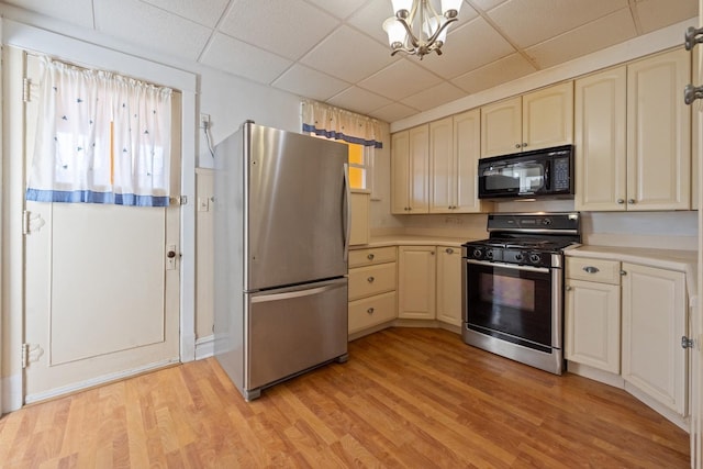 kitchen featuring light wood-type flooring, stainless steel appliances, a drop ceiling, and a notable chandelier