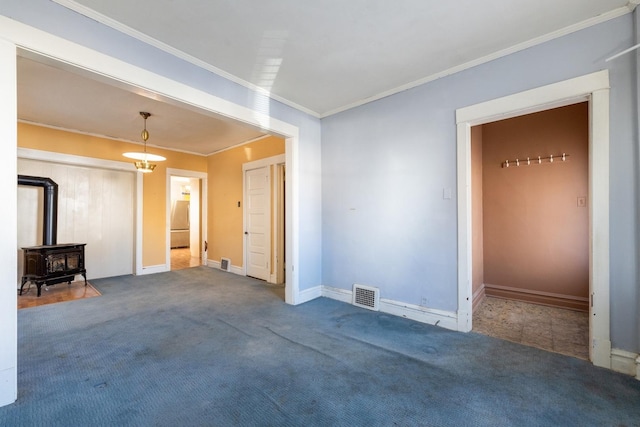 carpeted spare room with a wood stove and crown molding