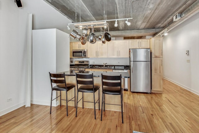 kitchen featuring sink, light wood-type flooring, a kitchen breakfast bar, rail lighting, and stainless steel appliances