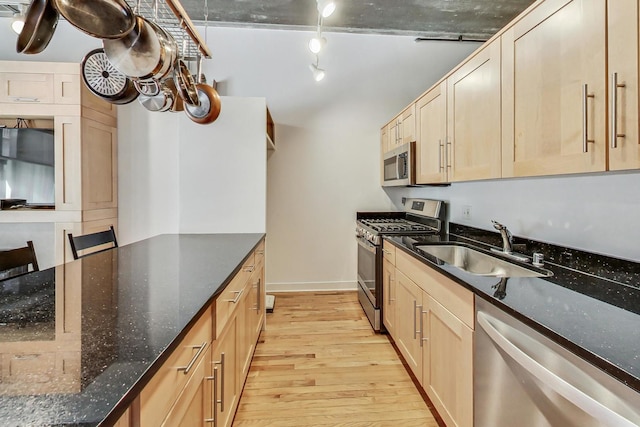 kitchen featuring light brown cabinetry, light hardwood / wood-style flooring, dark stone countertops, sink, and stainless steel appliances