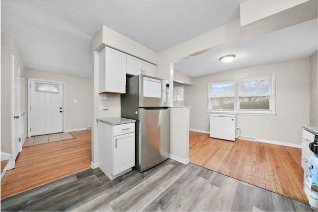 kitchen featuring white cabinets, light stone counters, light wood-type flooring, and stainless steel refrigerator