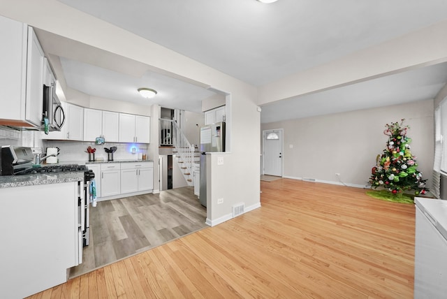 kitchen with light stone countertops, white range with gas stovetop, backsplash, light hardwood / wood-style floors, and white cabinets