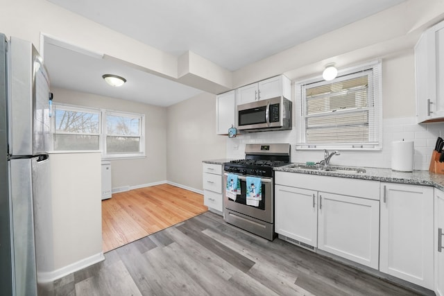 kitchen featuring backsplash, sink, light hardwood / wood-style flooring, appliances with stainless steel finishes, and white cabinetry