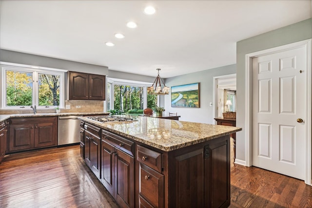 kitchen with appliances with stainless steel finishes, a kitchen island, dark brown cabinets, dark hardwood / wood-style flooring, and decorative light fixtures