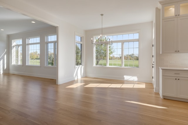 unfurnished dining area featuring an inviting chandelier, ornamental molding, and light wood-type flooring