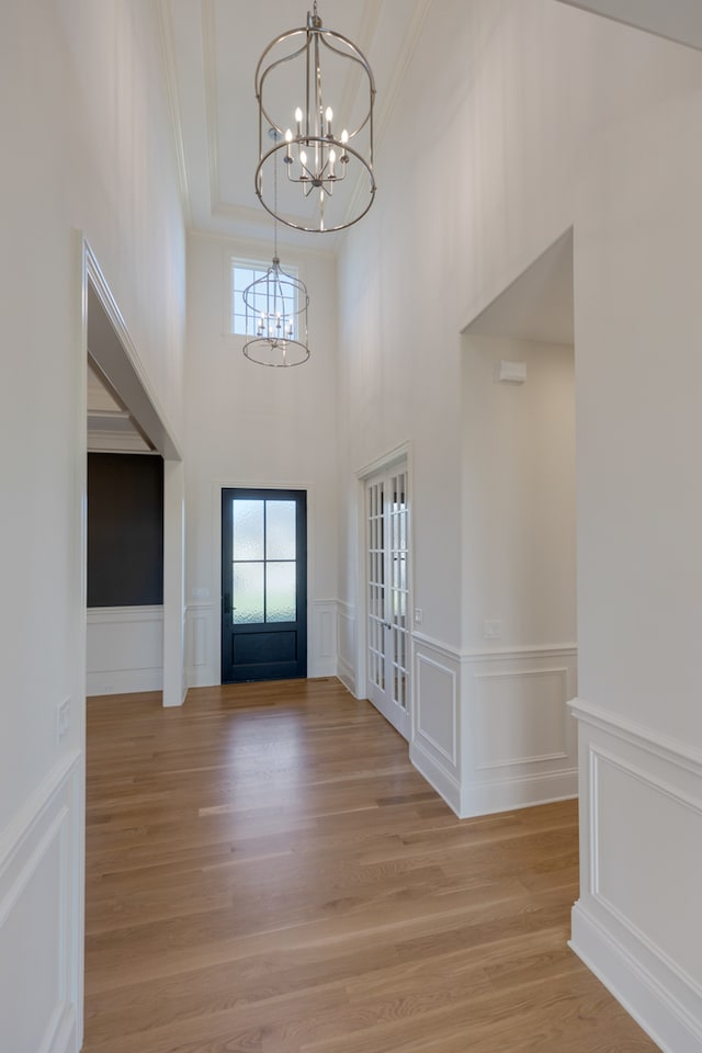 foyer featuring french doors, a high ceiling, crown molding, a notable chandelier, and light hardwood / wood-style flooring