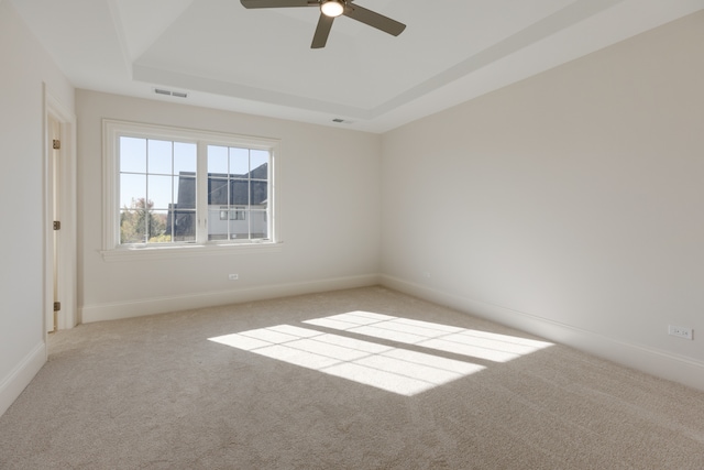 spare room with light carpet, a tray ceiling, and ceiling fan